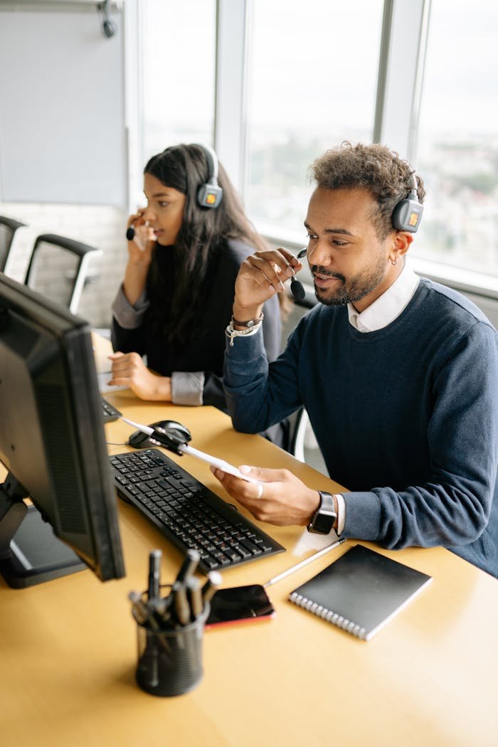 Two diverse call center agents working together at their desks with headsets in a bright office.